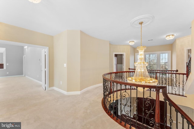 hall featuring baseboards, a chandelier, carpet flooring, and an upstairs landing