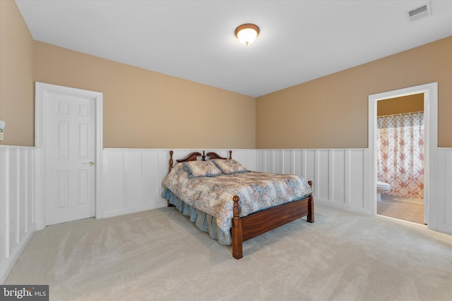 bedroom with carpet floors, visible vents, connected bathroom, and wainscoting