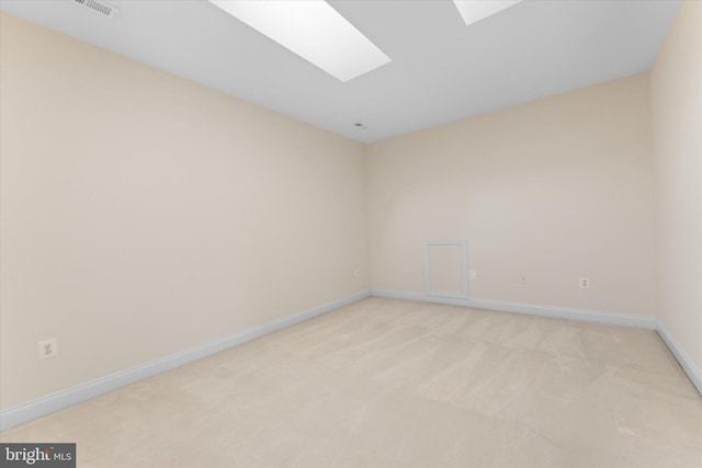 empty room with a skylight, light colored carpet, and baseboards