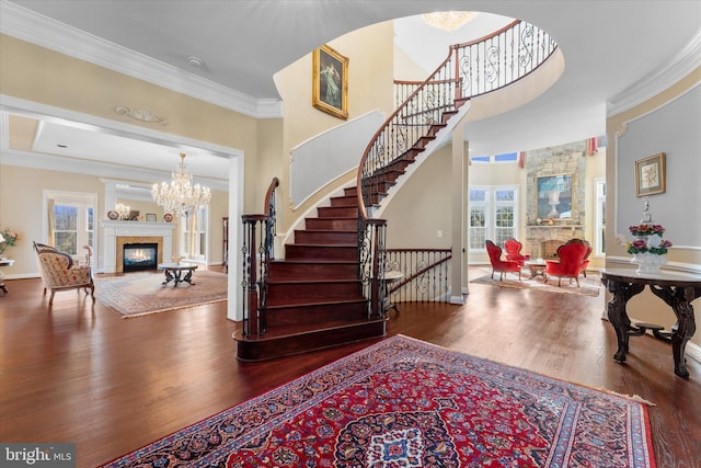 entryway with a premium fireplace, stairway, ornamental molding, wood finished floors, and a notable chandelier