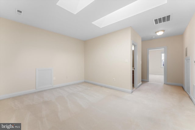 empty room featuring a skylight, visible vents, light carpet, and baseboards