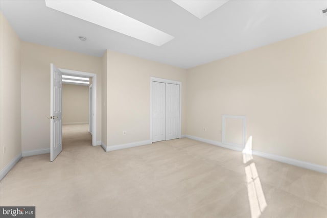 unfurnished bedroom featuring light carpet, a skylight, baseboards, and a closet