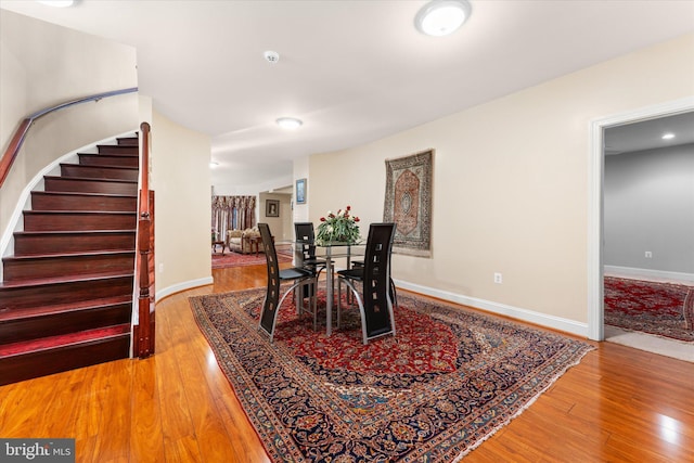 dining space featuring stairs, light wood-type flooring, and baseboards