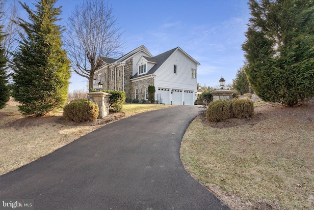 view of side of home featuring an attached garage, stone siding, and aphalt driveway