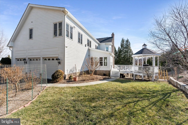 rear view of house featuring a lawn, a gazebo, fence, a deck, and a garage