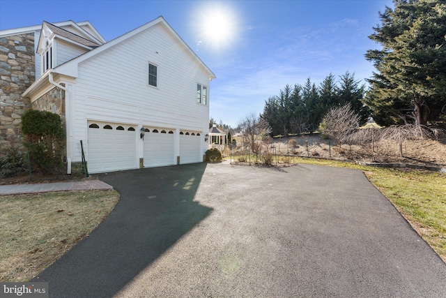 view of property exterior with an attached garage, stone siding, and aphalt driveway