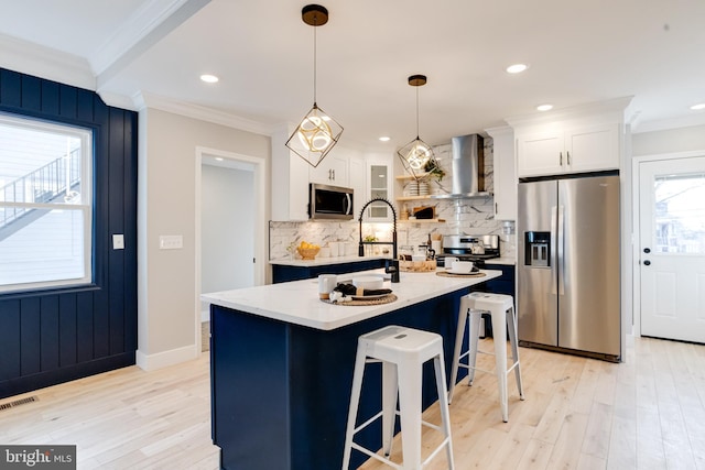 kitchen with stainless steel appliances, wall chimney range hood, white cabinets, and decorative light fixtures