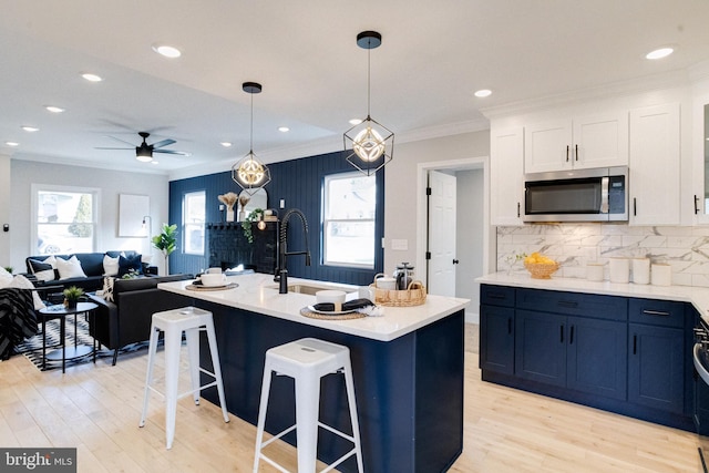 kitchen featuring sink, crown molding, hanging light fixtures, an island with sink, and white cabinets