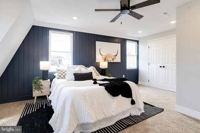 bedroom with ceiling fan, carpet flooring, multiple windows, and wood walls