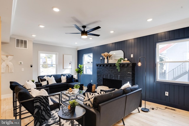 living room featuring crown molding, a brick fireplace, ceiling fan, and light wood-type flooring