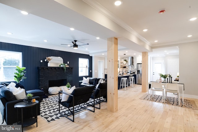 living room featuring a healthy amount of sunlight, ornamental molding, a fireplace, and light hardwood / wood-style floors