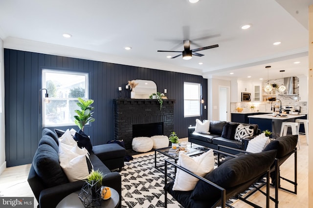 living room featuring crown molding, ceiling fan, a fireplace, and light hardwood / wood-style flooring