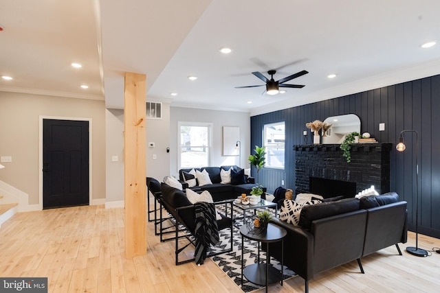 living room with crown molding, ceiling fan, light hardwood / wood-style floors, and a brick fireplace