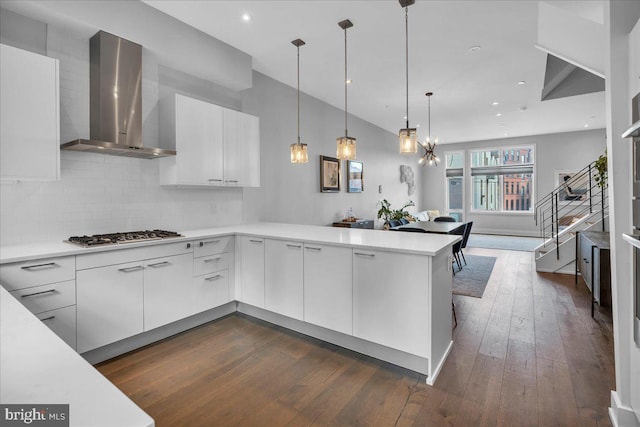 kitchen featuring stainless steel gas stovetop, kitchen peninsula, white cabinets, and wall chimney exhaust hood