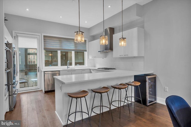 kitchen featuring wine cooler, wall chimney exhaust hood, white cabinetry, appliances with stainless steel finishes, and kitchen peninsula