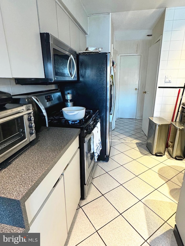 kitchen featuring stainless steel appliances, light tile patterned floors, and white cabinets