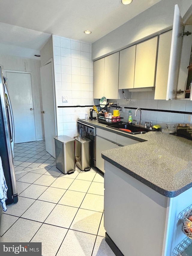 kitchen with tasteful backsplash, sink, tile walls, stainless steel fridge, and kitchen peninsula