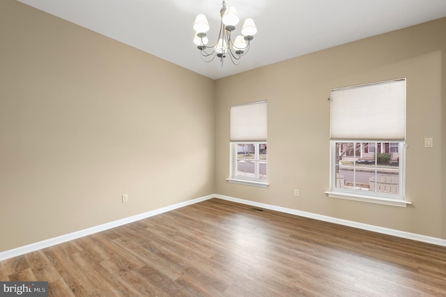 spare room with a healthy amount of sunlight, hardwood / wood-style flooring, and a chandelier