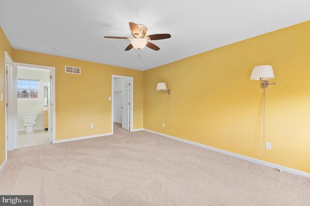 unfurnished bedroom featuring carpet floors, a spacious closet, ceiling fan, ensuite bath, and a closet