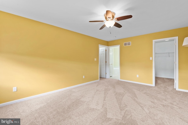 unfurnished bedroom with light carpet, a walk in closet, a closet, and ceiling fan