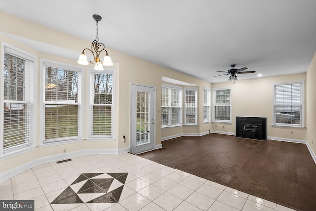 unfurnished living room featuring ceiling fan with notable chandelier, a healthy amount of sunlight, and light tile patterned flooring