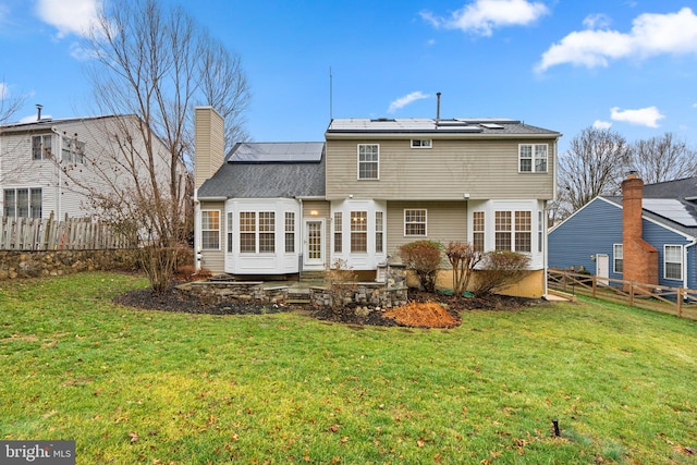 rear view of property featuring a yard and solar panels