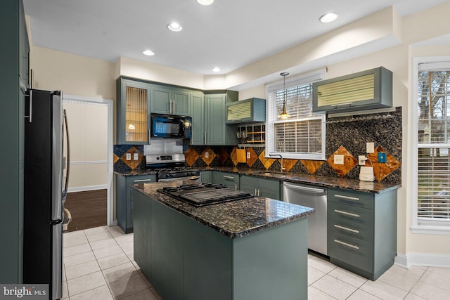 kitchen featuring green cabinets, appliances with stainless steel finishes, a kitchen island, decorative light fixtures, and dark stone counters