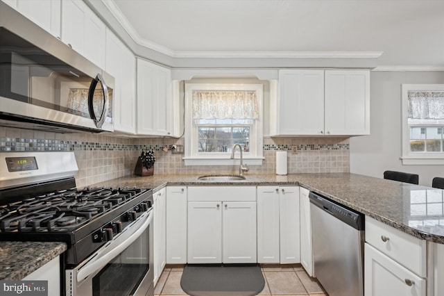 kitchen featuring sink, white cabinetry, ornamental molding, appliances with stainless steel finishes, and dark stone counters