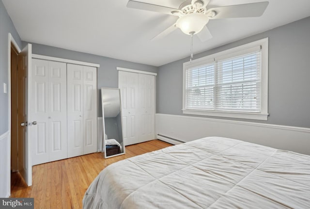 bedroom with two closets, a baseboard radiator, ceiling fan, and hardwood / wood-style flooring