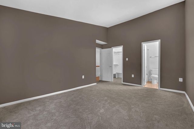 unfurnished bedroom featuring connected bathroom, a spacious closet, light colored carpet, and a closet