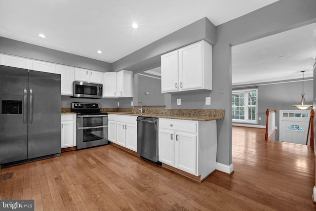 kitchen with appliances with stainless steel finishes, white cabinetry, dark stone countertops, light hardwood / wood-style floors, and decorative light fixtures