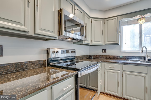 kitchen with sink, gray cabinetry, dark stone counters, light tile patterned floors, and stainless steel appliances