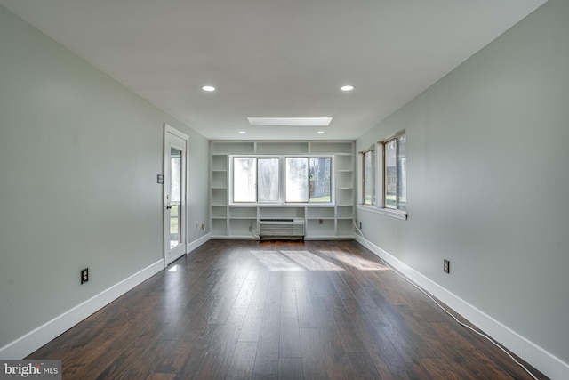 unfurnished living room featuring built in shelves, dark wood-type flooring, a wall mounted AC, and a skylight