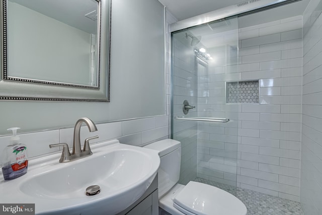 bathroom featuring a shower with door, vanity, tile walls, and toilet