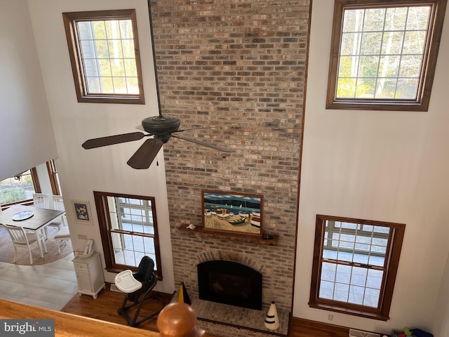 living room with a brick fireplace, hardwood / wood-style floors, a healthy amount of sunlight, and a high ceiling