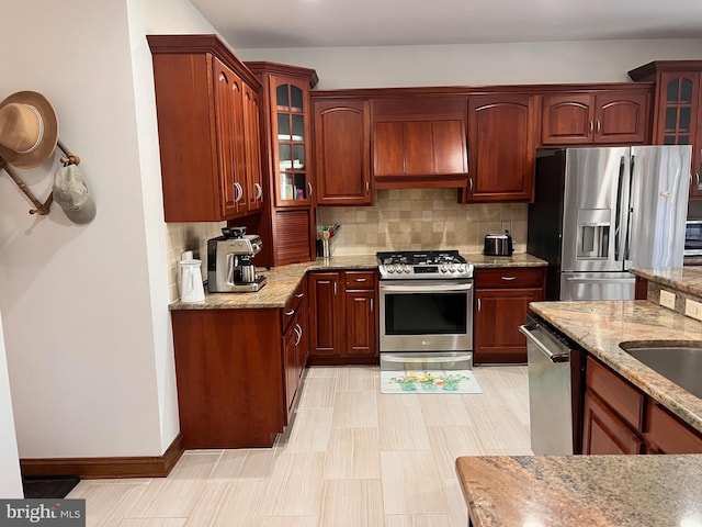 kitchen featuring tasteful backsplash, wall chimney range hood, light stone counters, and appliances with stainless steel finishes