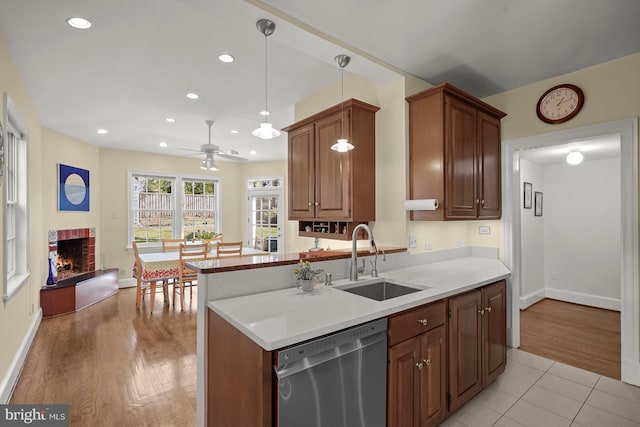 kitchen with a fireplace, decorative light fixtures, sink, stainless steel dishwasher, and kitchen peninsula