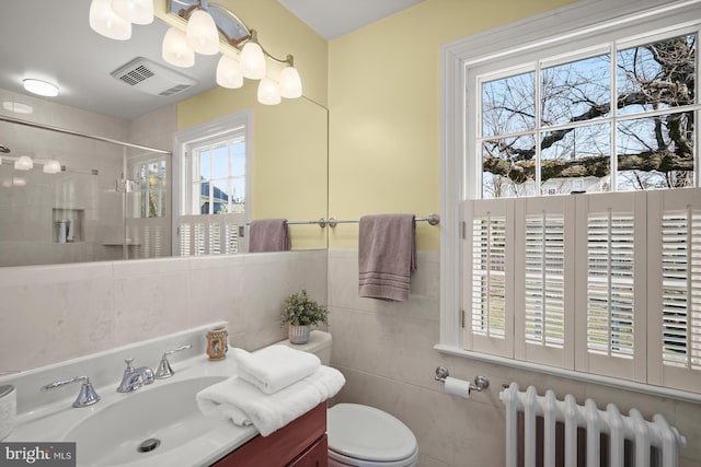 bathroom with radiator, tile walls, tiled shower, vanity, and toilet