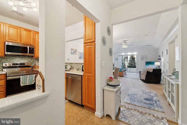 kitchen featuring lofted ceiling, tasteful backsplash, light tile patterned floors, appliances with stainless steel finishes, and ceiling fan with notable chandelier