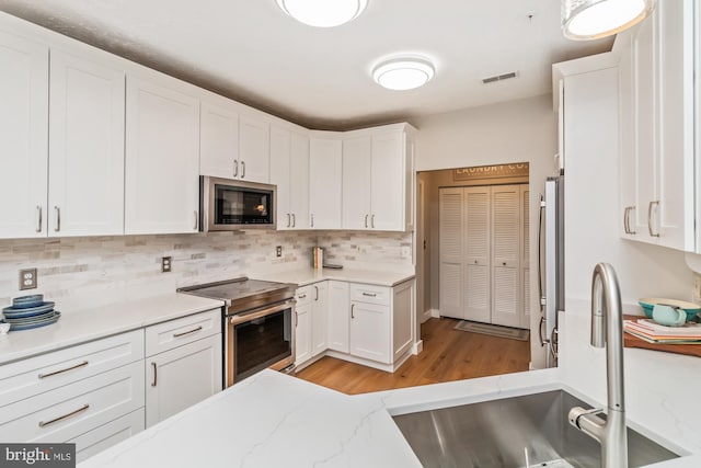 kitchen featuring sink, light hardwood / wood-style flooring, appliances with stainless steel finishes, white cabinetry, and decorative backsplash