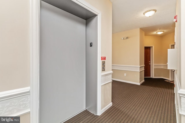 hallway with elevator and dark carpet