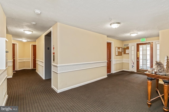 hall featuring a textured ceiling and dark carpet