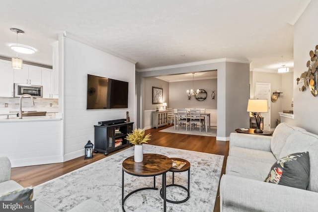 living room featuring crown molding, sink, dark wood-type flooring, and a chandelier