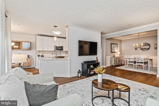 living room featuring ornamental molding, dark hardwood / wood-style floors, sink, and a notable chandelier