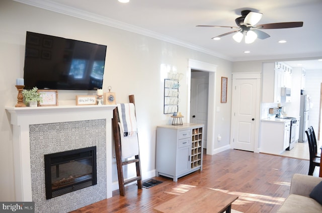 living room with ornamental molding, a tile fireplace, and wood-type flooring