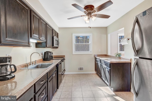 kitchen featuring dark brown cabinetry, sink, light tile patterned floors, appliances with stainless steel finishes, and ceiling fan