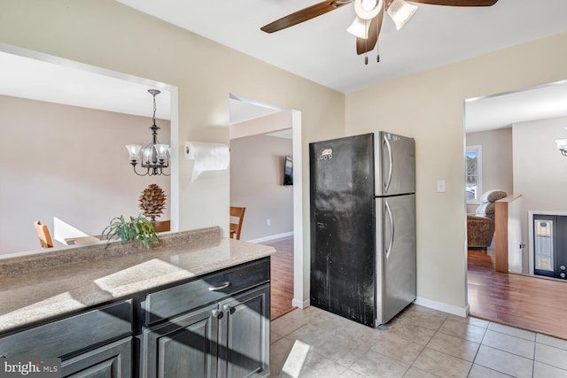 kitchen with ceiling fan with notable chandelier, stainless steel refrigerator, light stone countertops, light tile patterned flooring, and decorative light fixtures