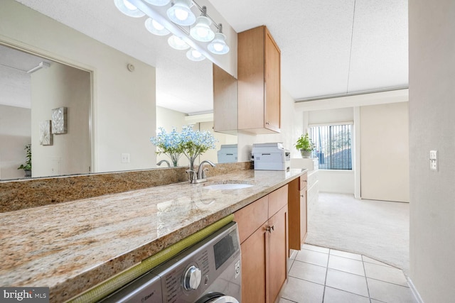 kitchen featuring washer / dryer, sink, a textured ceiling, light carpet, and light stone countertops