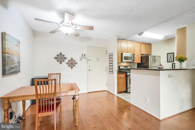 kitchen with light hardwood / wood-style floors, kitchen peninsula, a textured ceiling, and appliances with stainless steel finishes