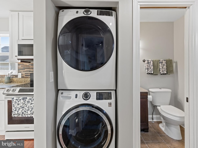 laundry room with dark tile patterned floors and stacked washer / dryer